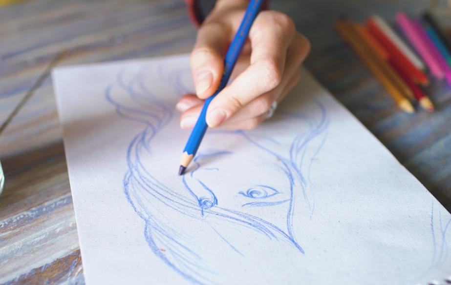 An artist sketches a woman on a white piece of paper with a blue colored pencil